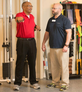 senior man using exercise machine with a rehab therapist