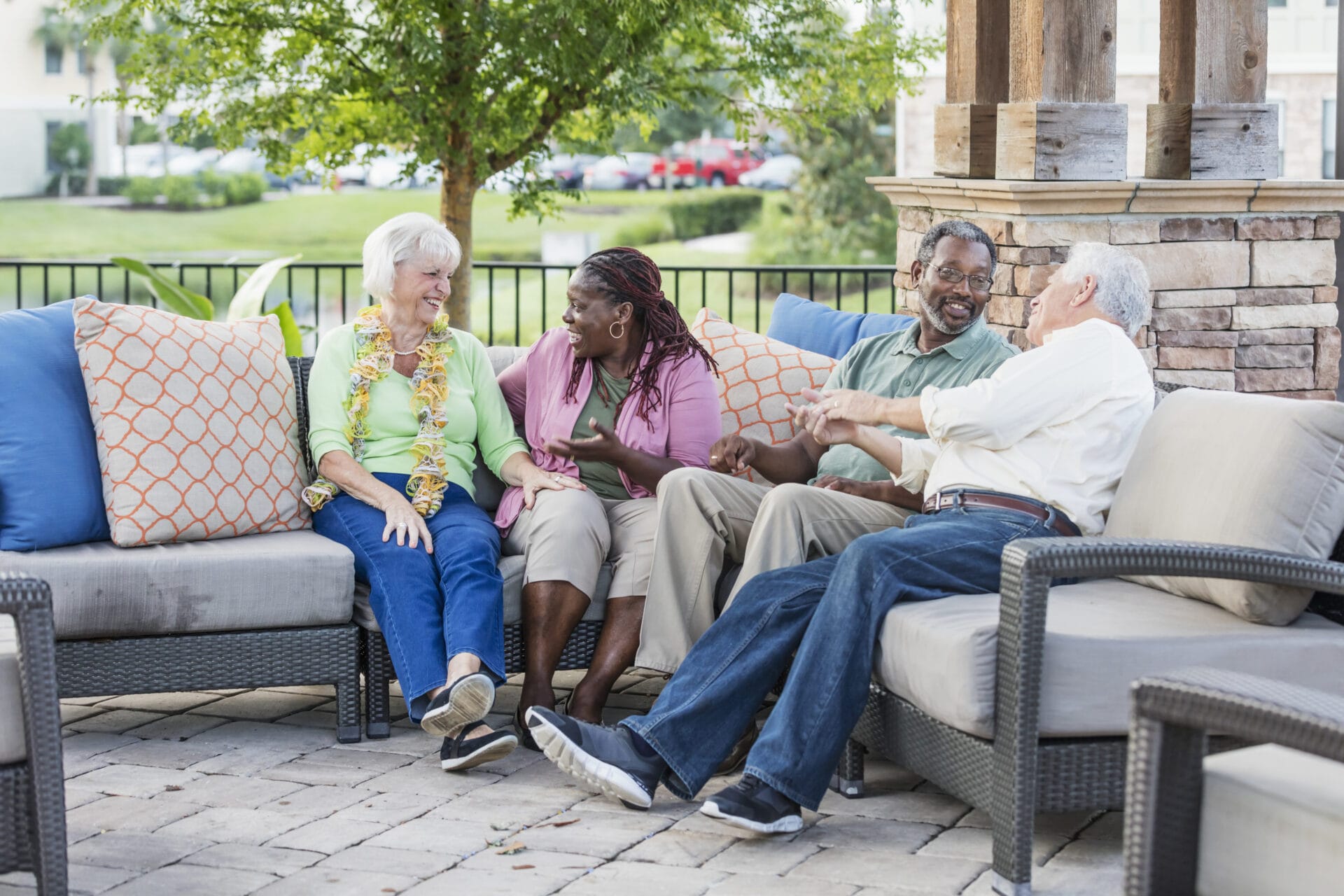 Four older adults sit outdoors on a patio having lively conversation.
