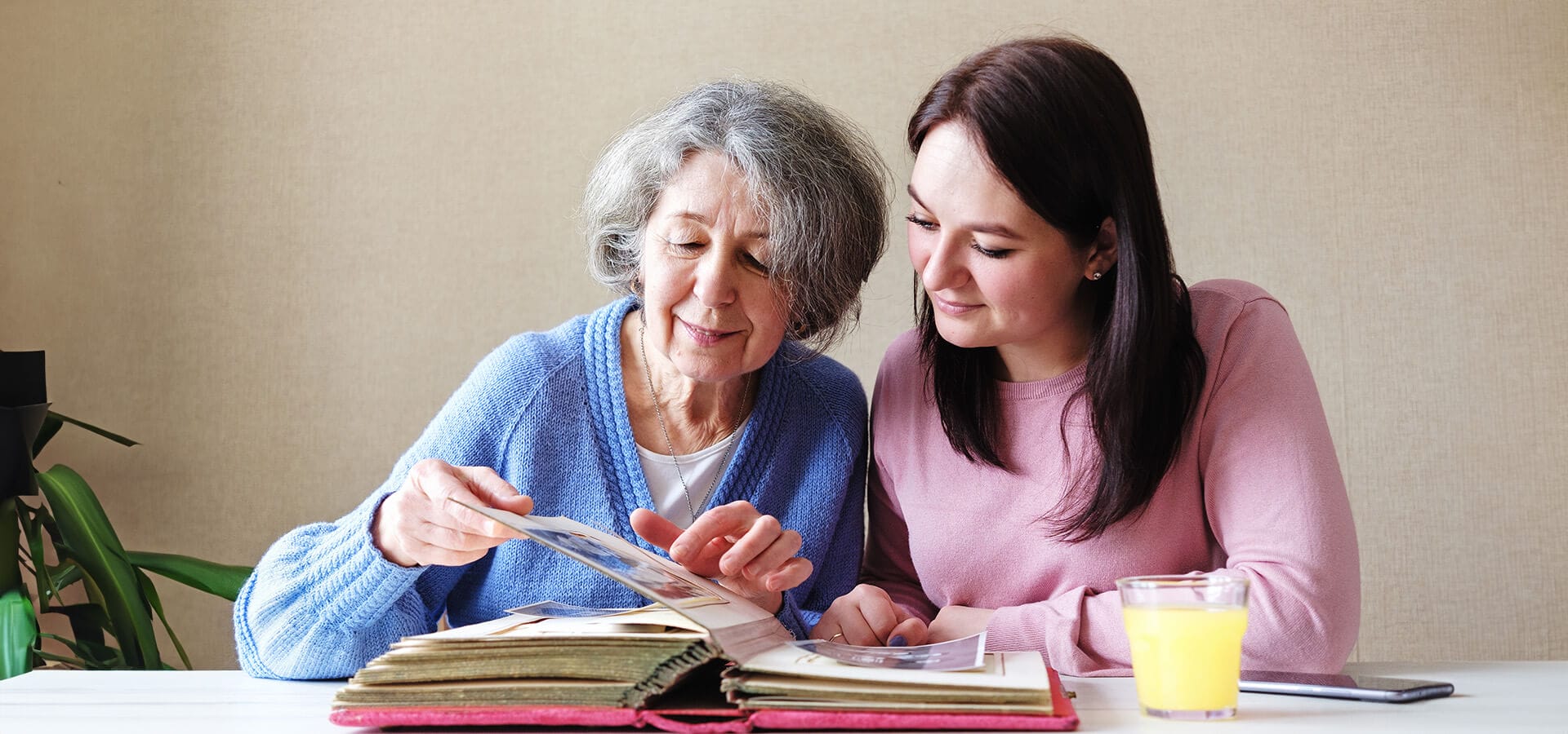 senior woman and her adult daughter look through photo albums together