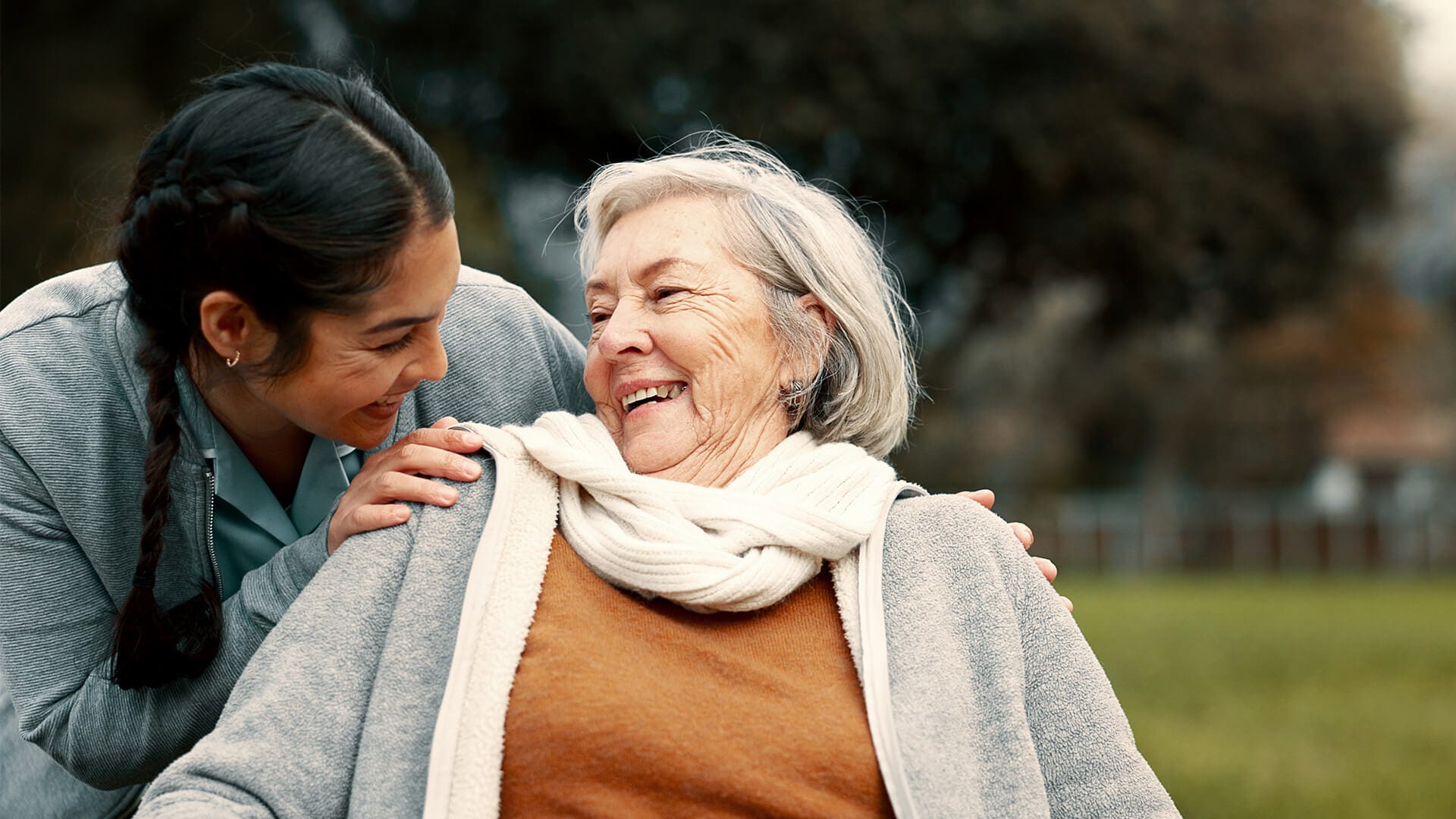 Caregiver smiles over elderly woman's shoulder.