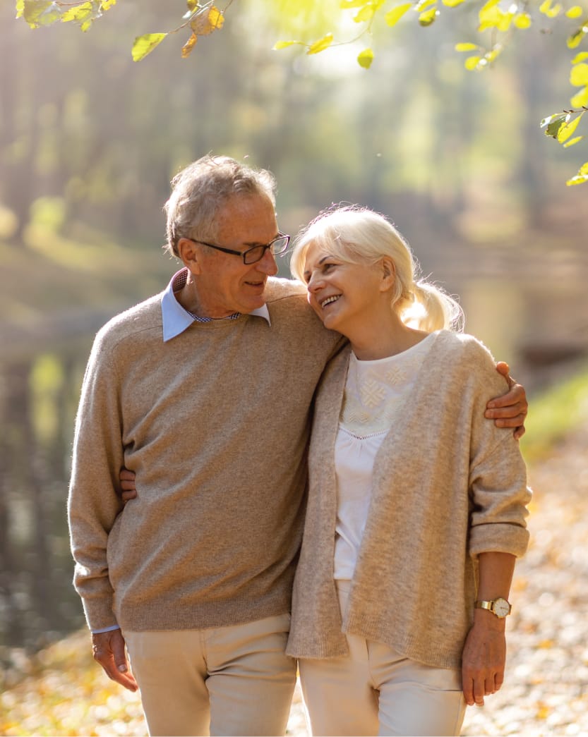 senior couple walking through an outdoor path covered in fall leaves