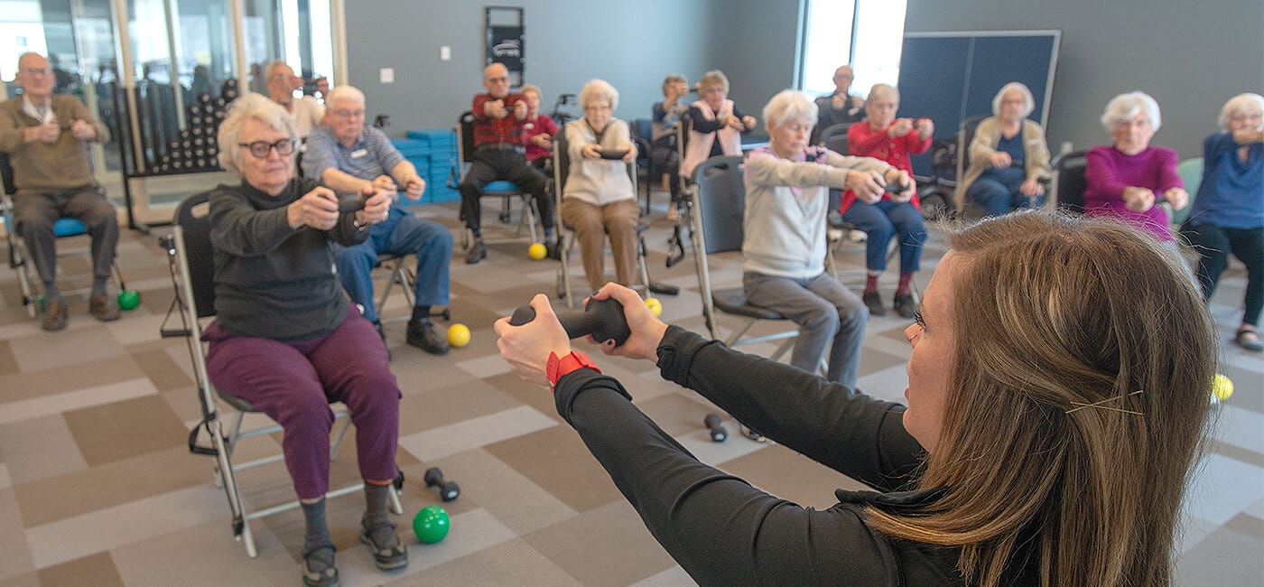 Fitness instructor leads group of seniors sitting in chairs and lifting hand weights