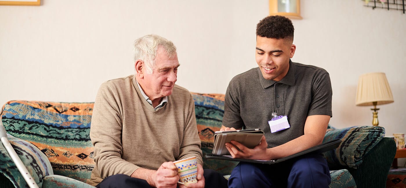 Senior man reviews information on a clipboard, while sitting on a couch with younger man