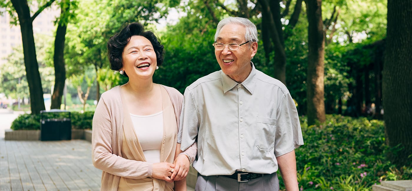 Senior man and woman link arms while walking on path outdoors